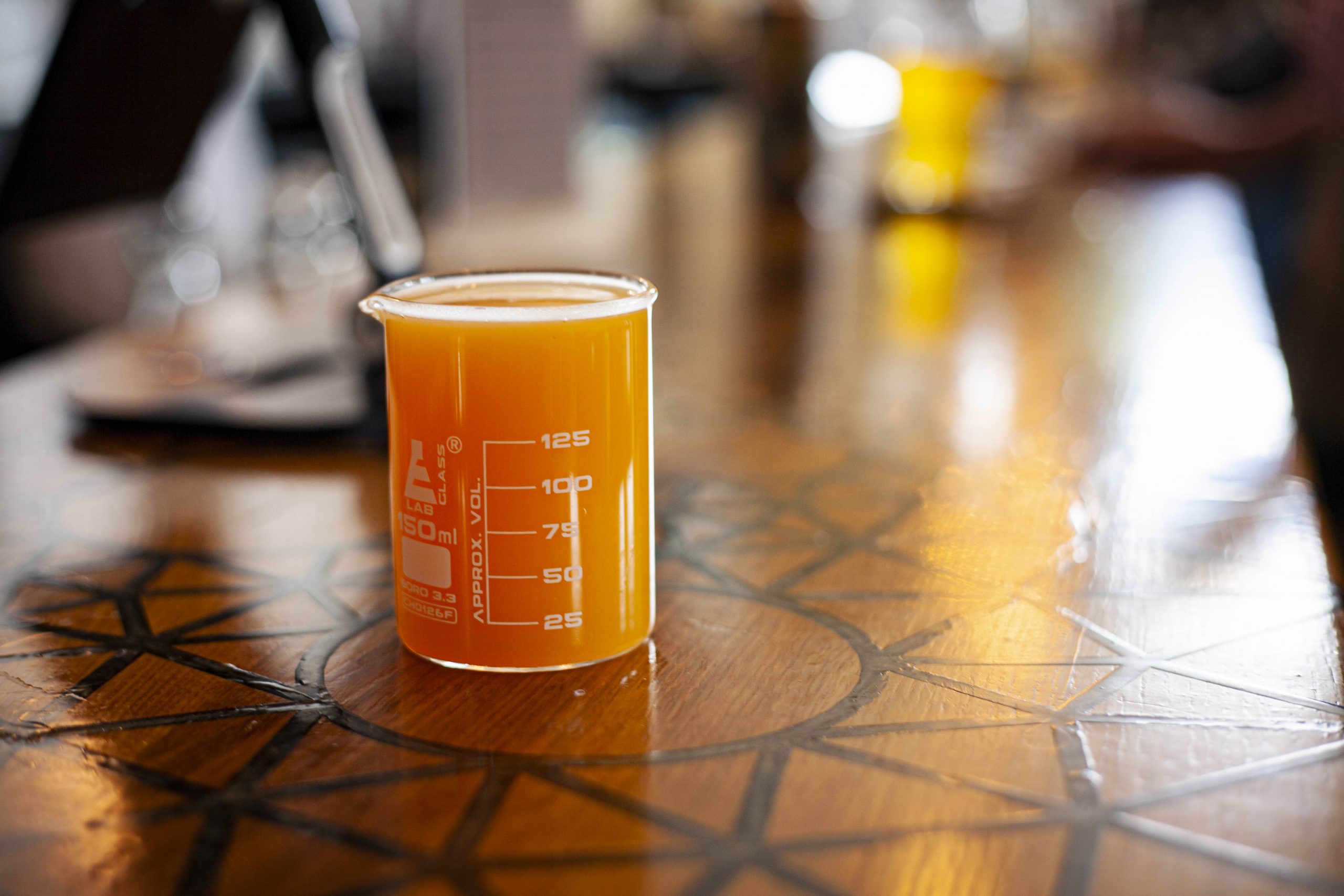 A bright orange fruit slushee beer is served in a four ounce scientific beaker