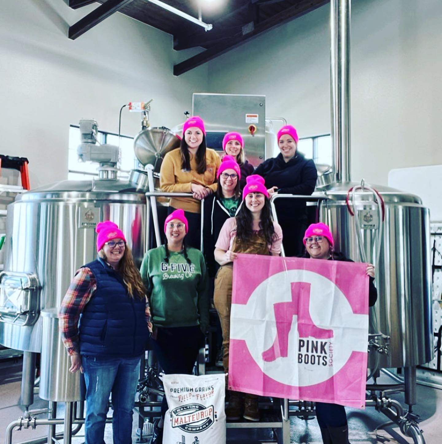 Smiling women in pink hats atop the brewhouse at Tumbled Rock Brewing