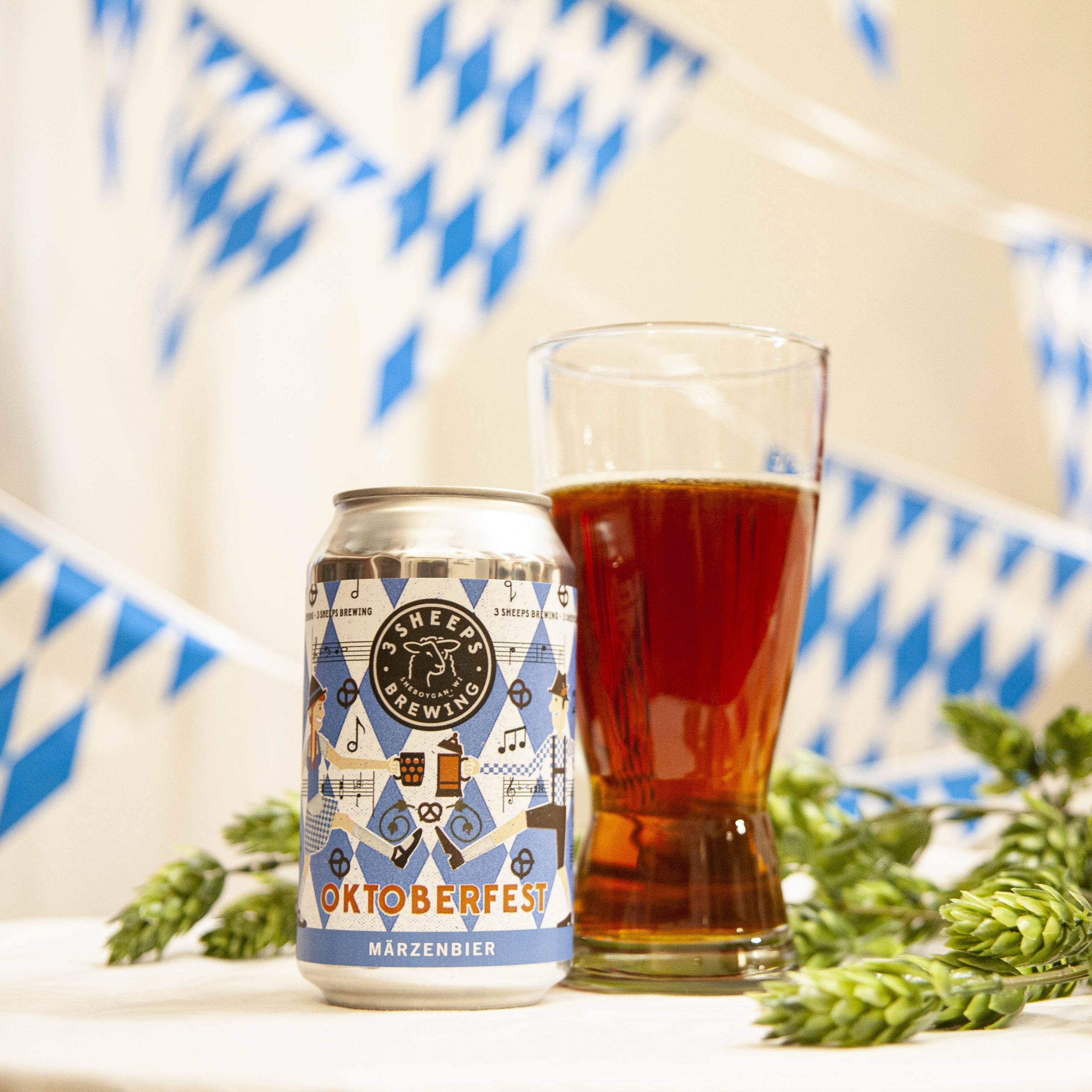 3 Sheeps' Oktoberfest Marzenbier is poured into a pilsner glass, amidst hop cones and blue and white bunting.