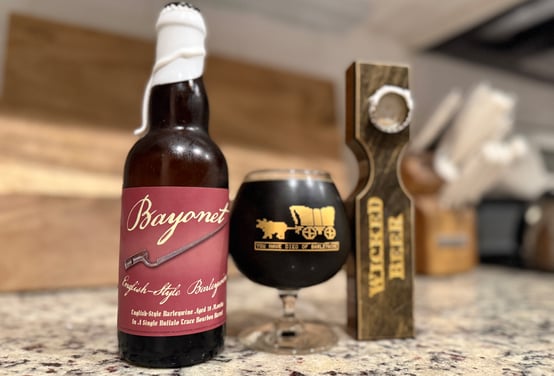 Review image of Jukes' Bayonet Barleywine tasting. White wax bottle, Oregon Trail-inspired barleywine snifter, custom bottle opener.