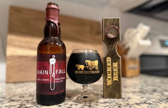 Review image of Jukes' Chain Fall Barleywine tasting. Red wax bottle, Oregon Trail-inspired barleywine snifter, custom bottle opener.