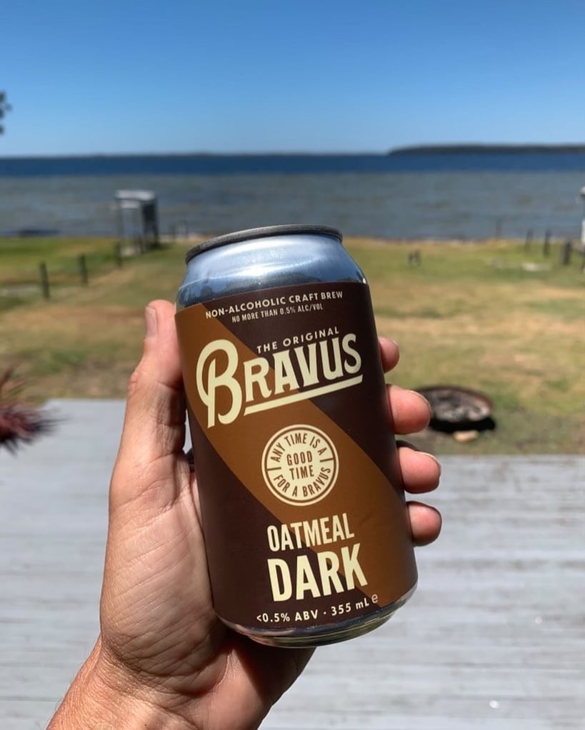 Bravus brewing co. oatmeal dark held in front of a seaside vista