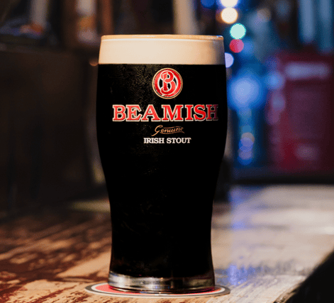 A pint of Beamish Genuine Irish Stout with a thick white head, sitting on a wooden bar.