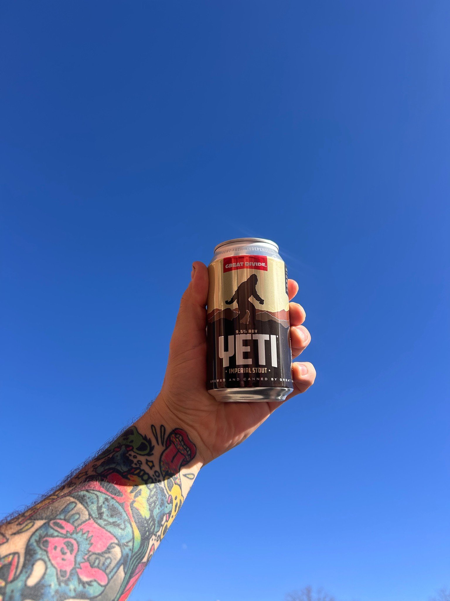 Great Divide Yeti Imperial Stout can held aloft in front of cloudless blue sky.