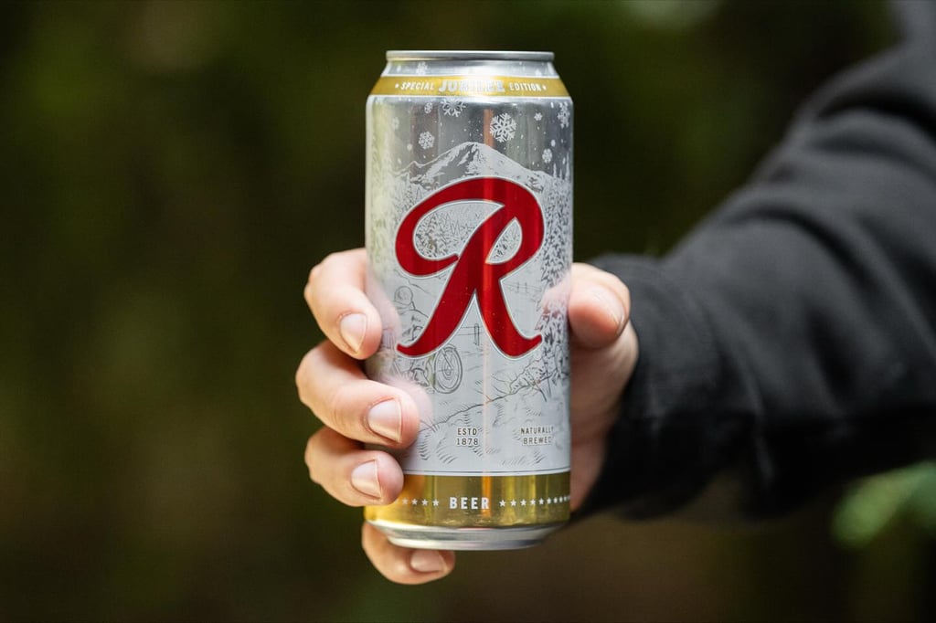 person holding can of rainier beer outdoors in wooded area