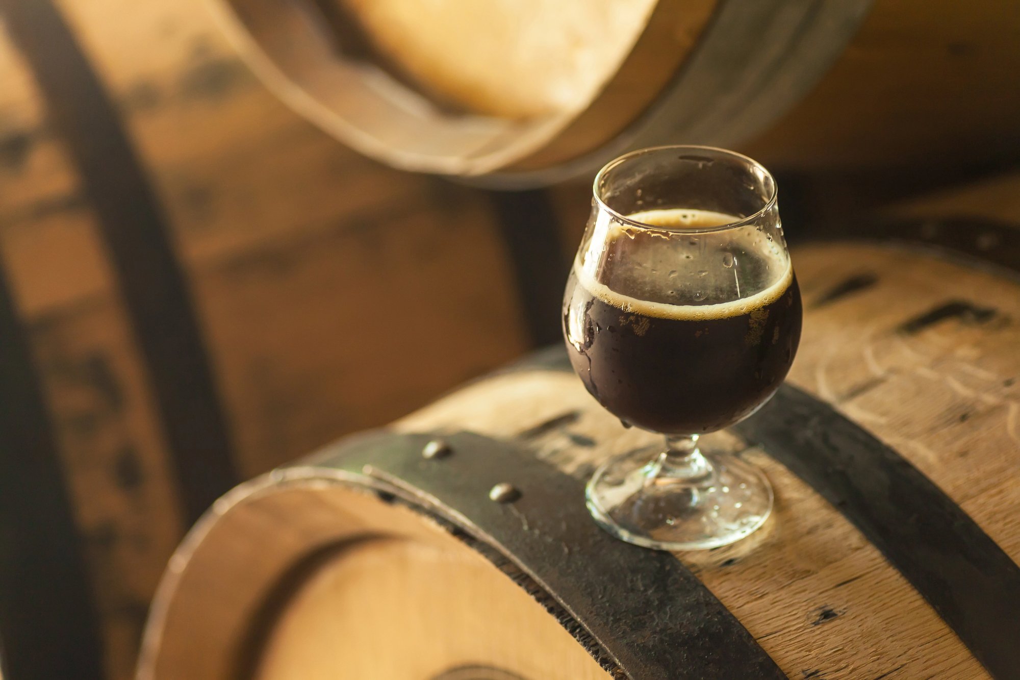 Glass of barrel-aged stout sitting on top of a barrel