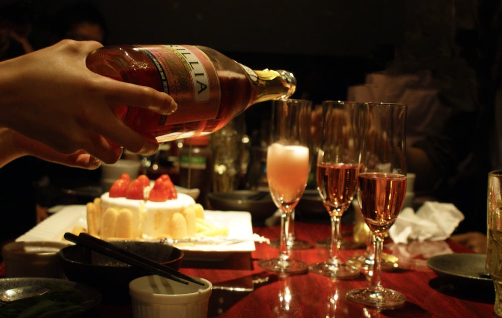 A hand pouring wine from a bottle into three glasses at a dinner table