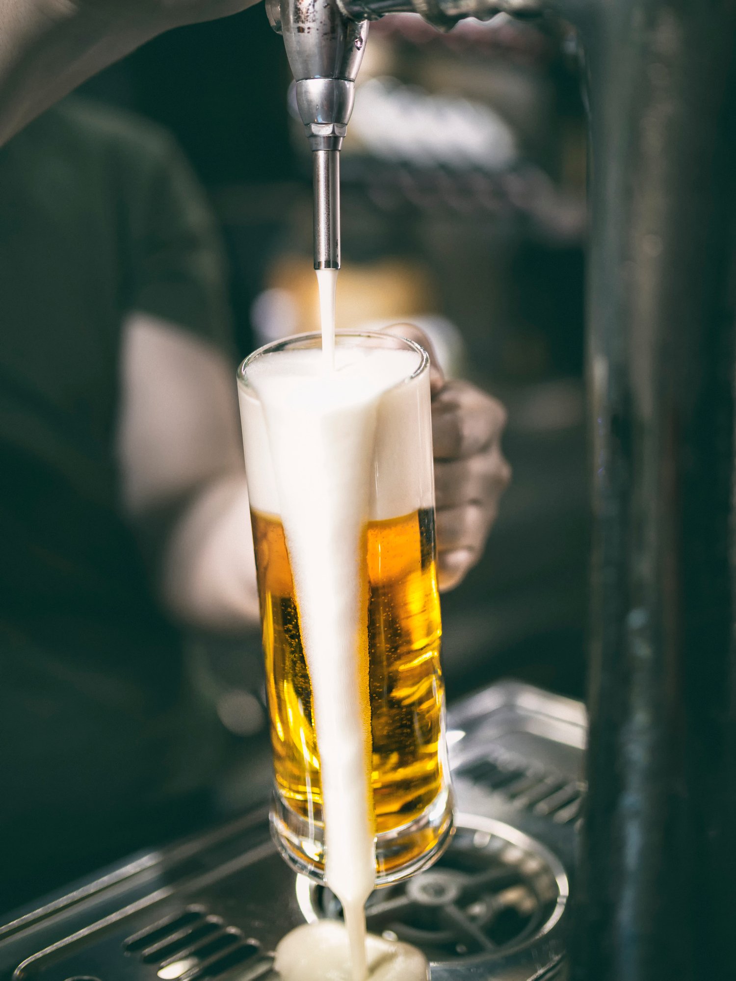 Glass of Pilsner beer overflowing with foam from the tap.