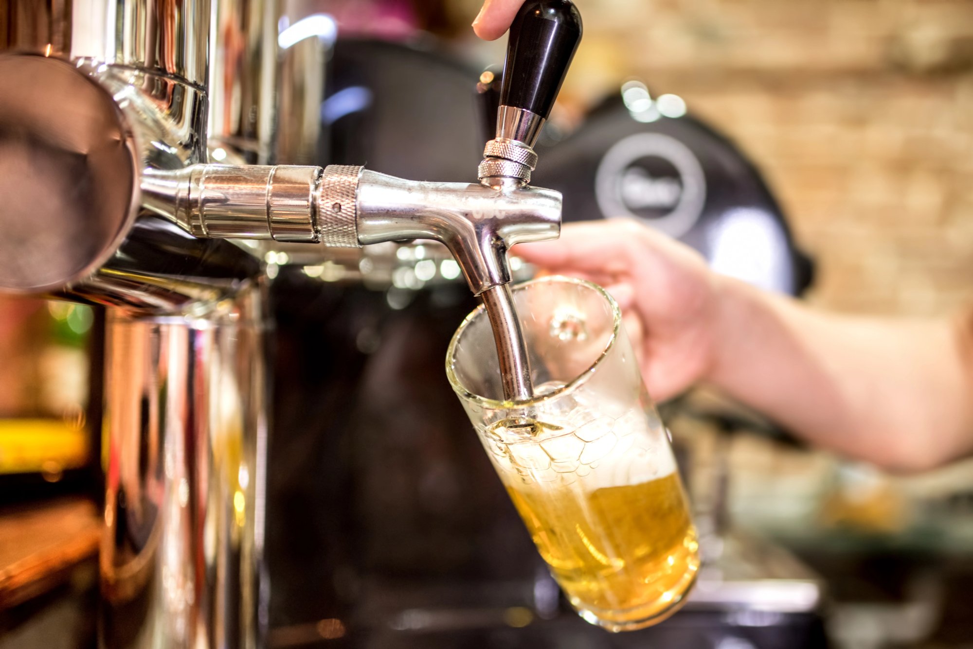 Mug of light beer being poured by a tap behind a bar