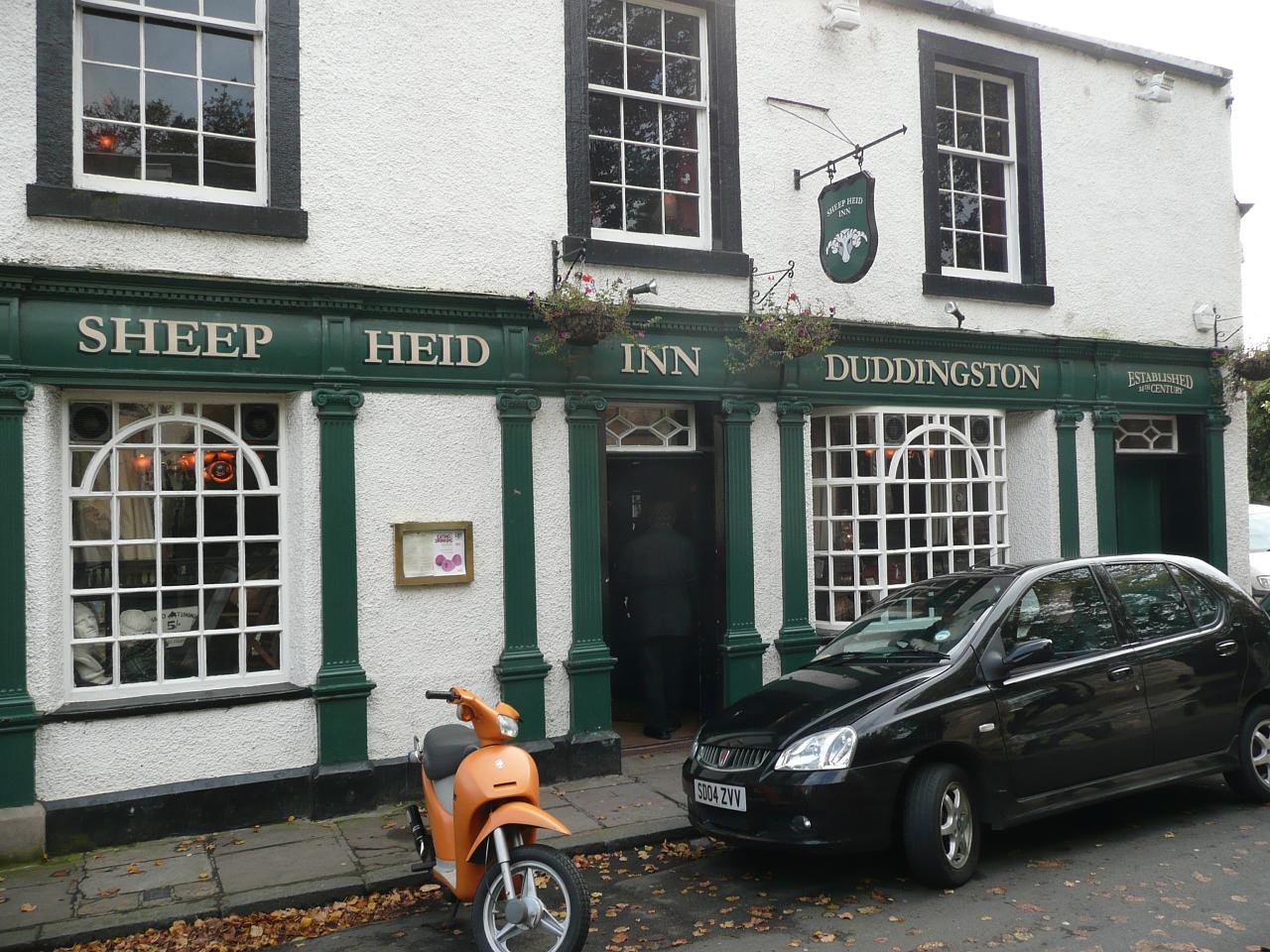 Street exterior of the Sheep Heid Inn with a car and a moped.