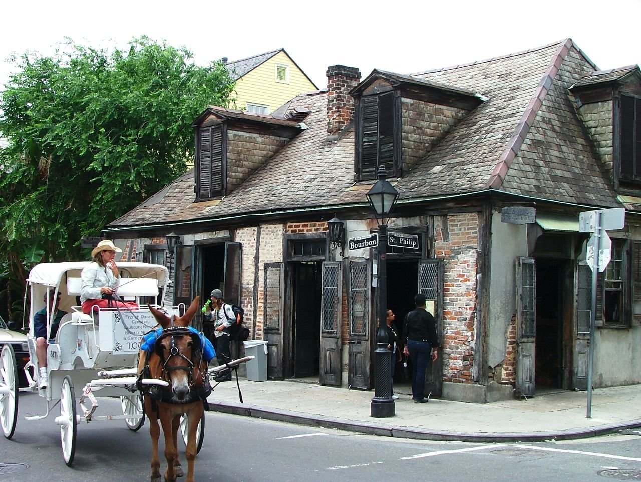 Exterior of Lafitte's Blacksmith Shop Bar, a small wooden building made of brick, with a horse-drawn carriage passing by.