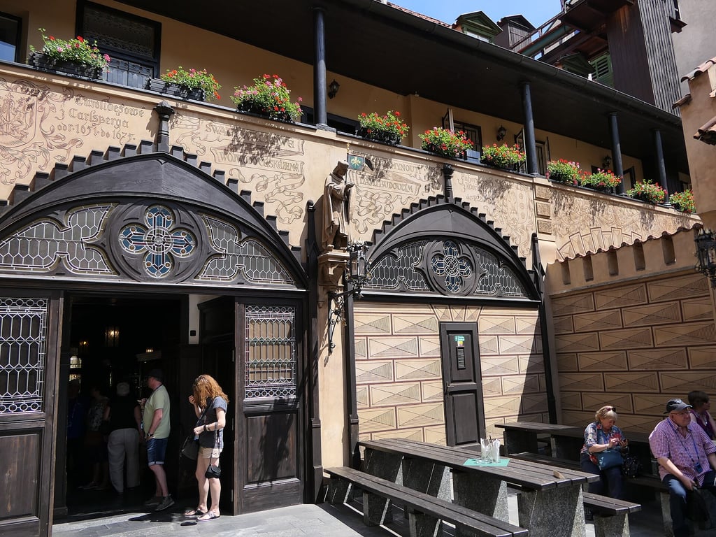 Courtyard at U Flecku, with a large wooden door, stained glass ornamentations, and benches for seating.