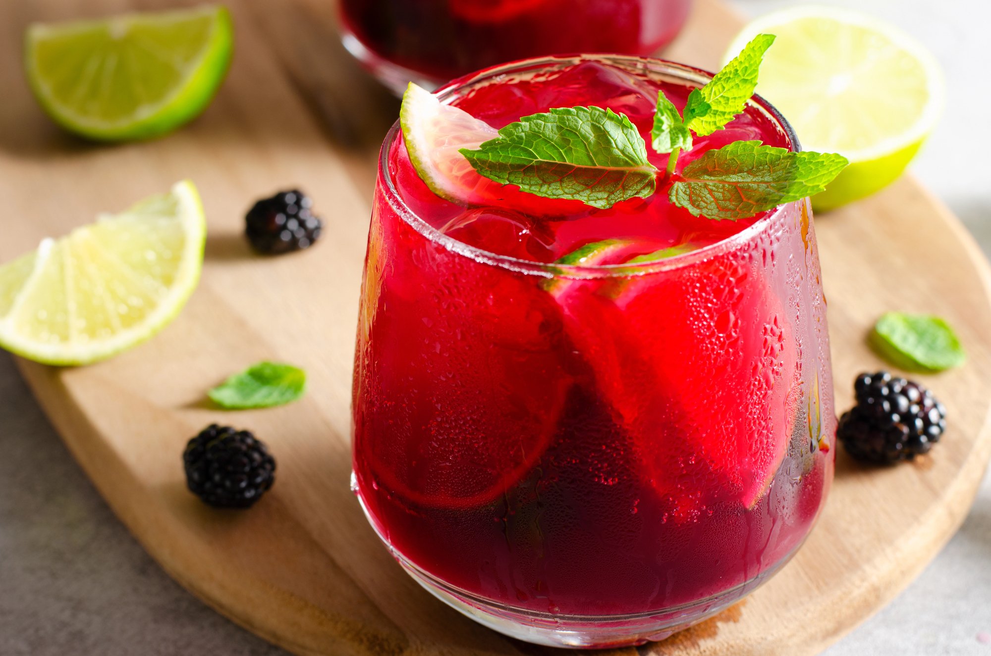 Glass of Porch Swing cocktail with sprig of mint and lime wedges with blackberries on serving tray.