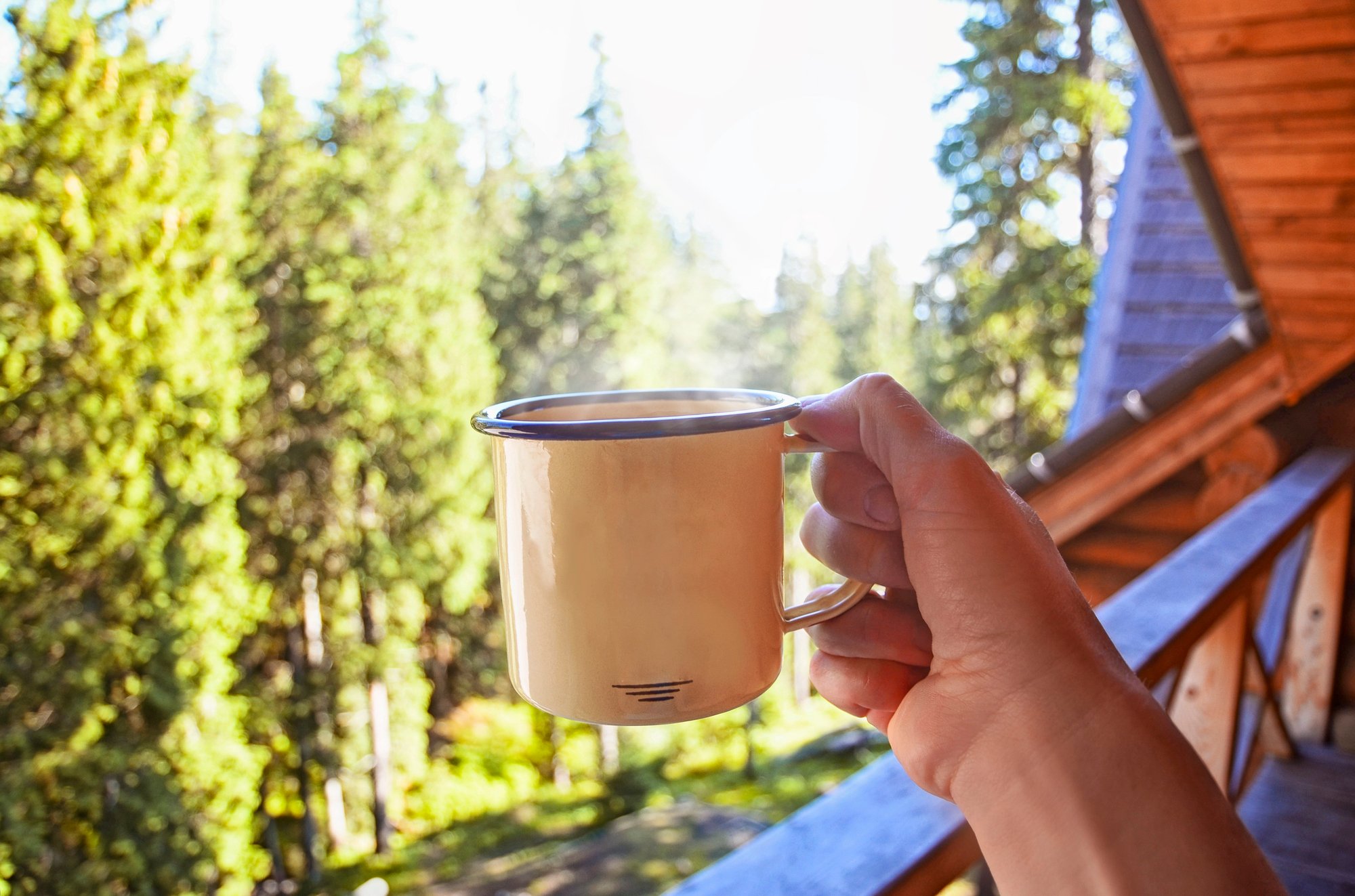 Person holding out steaming coffee mug before drinking it on the porch.
