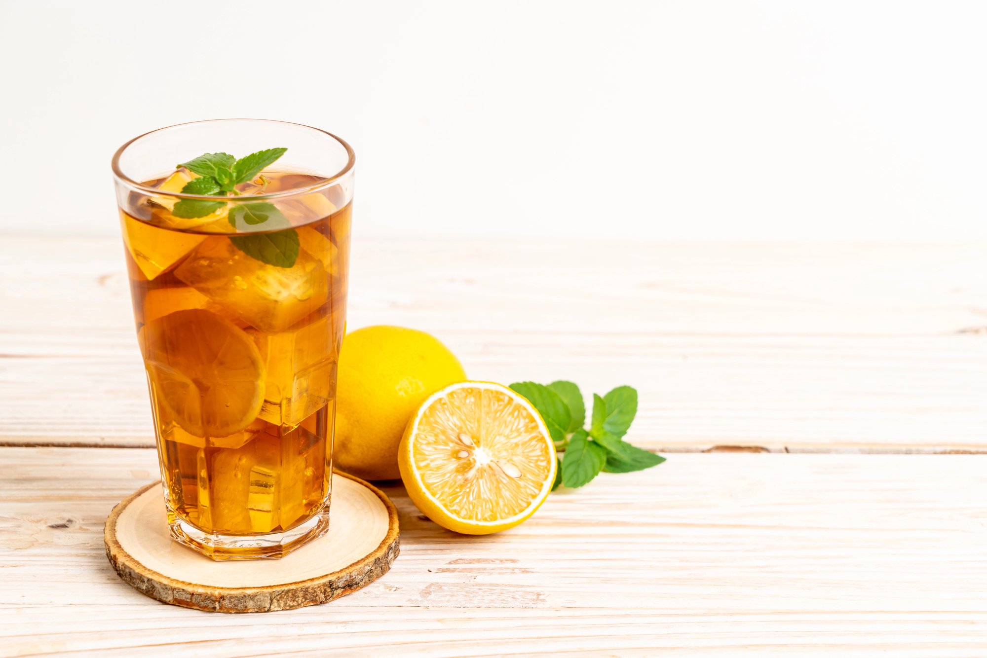Glass of front porch tea on wooden table with lemon wedges and sprig of mint.