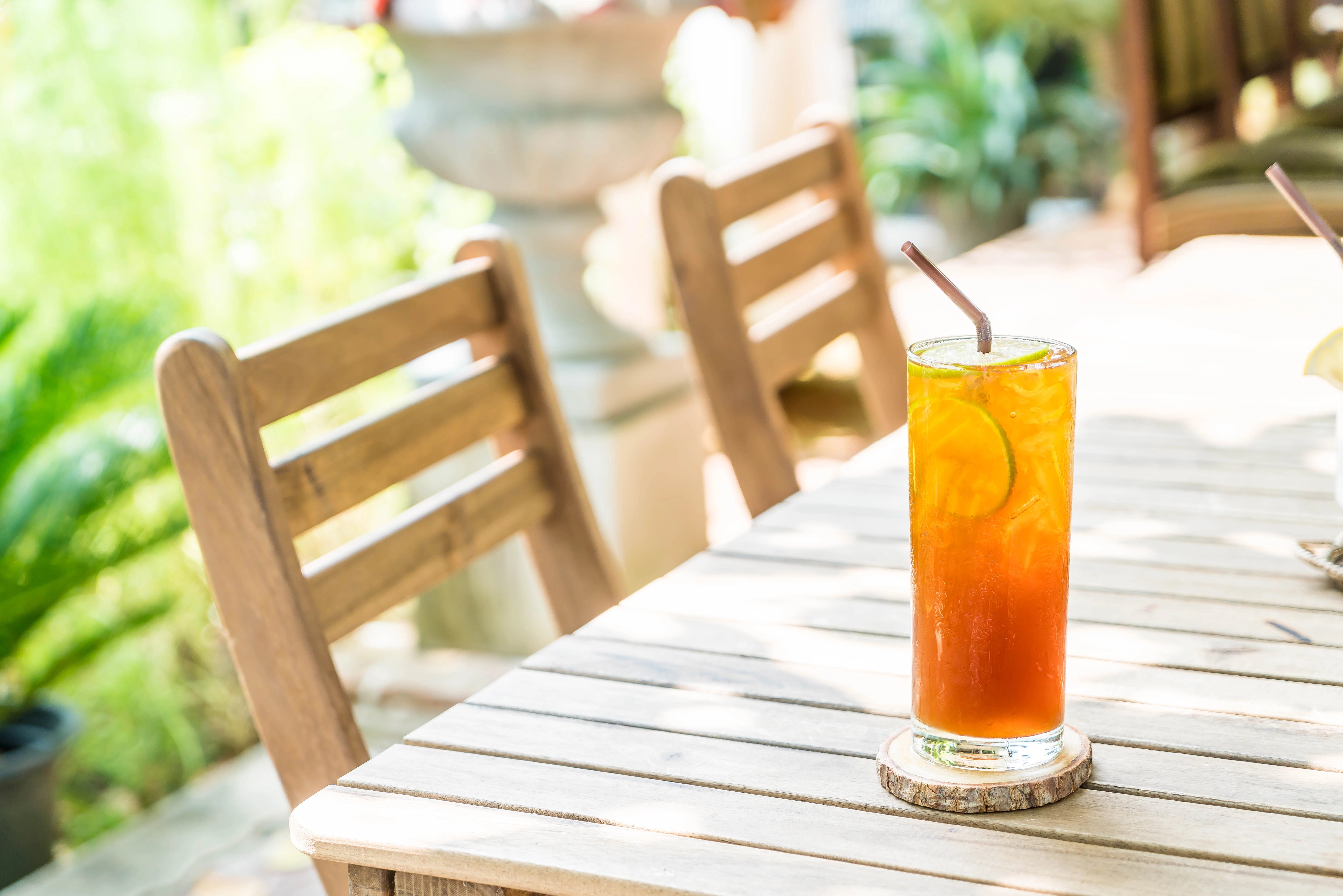 A porch drink on an outdoor table made with iced tea with a lime wedge and straw.