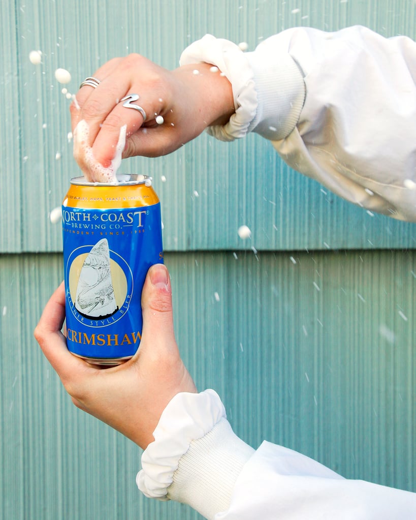 North Coast Brewing Co. Scrimshaw Pilsner can being opened forcefully outside with foam spewing forth.