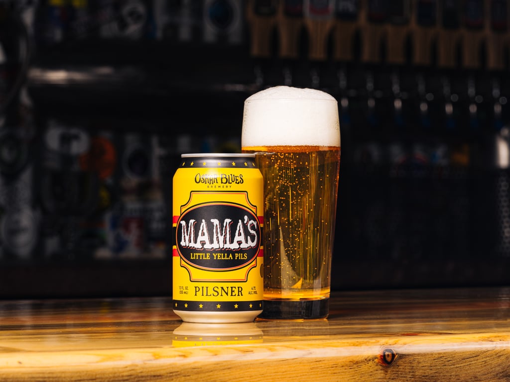 Oskar Blues Brewery Mama's Little Yella Pils can and glass in a bar.
