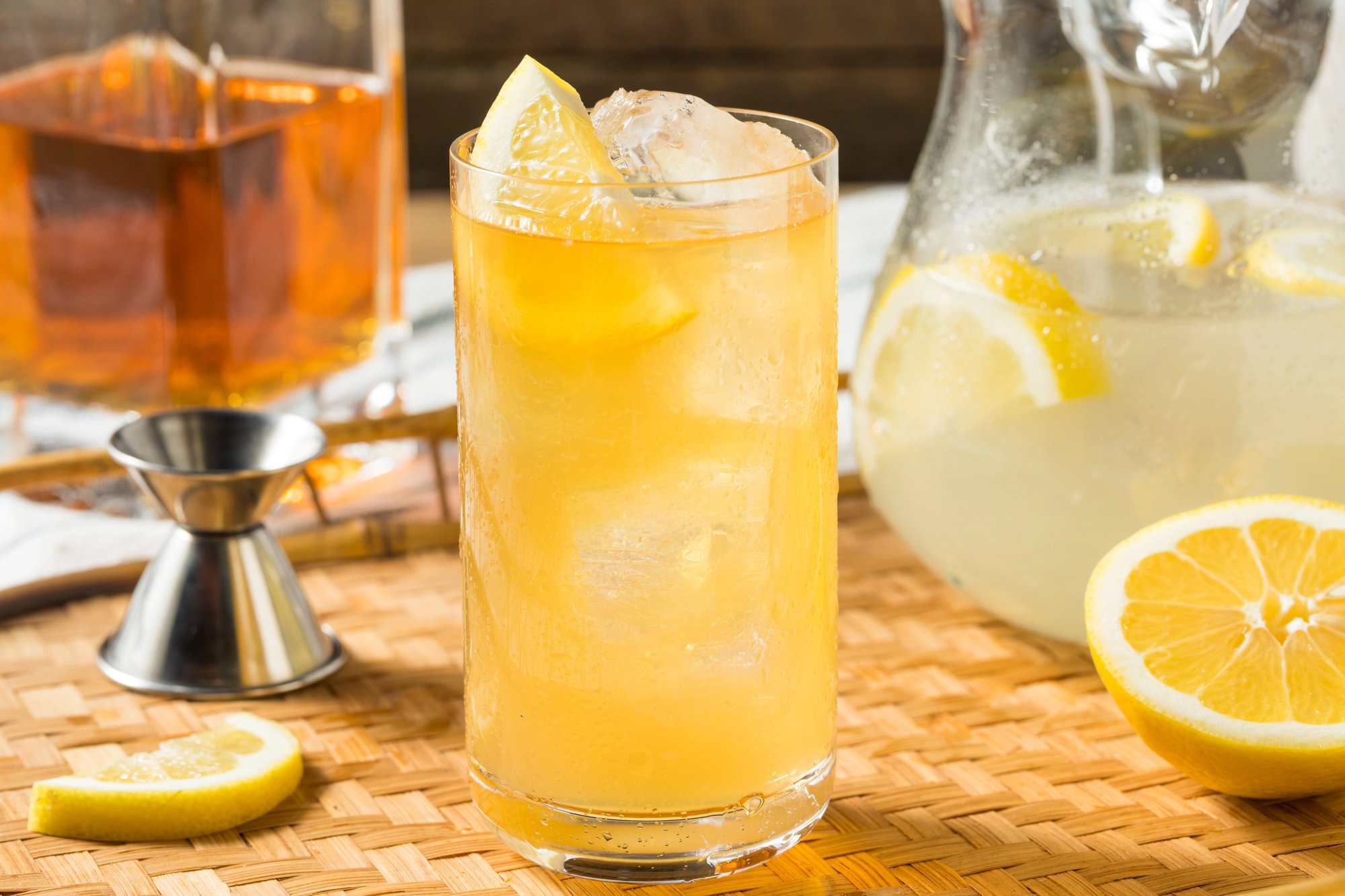 Glass of porch swing drink with bourbon, sweet tea, and lemonade next to shot glass, pitcher of lemonade, and bourbon decanter.