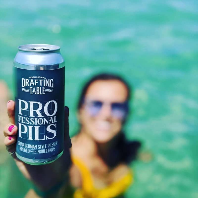 A girl holding a can of Professional Pils from Drafting Table Brewing Company.