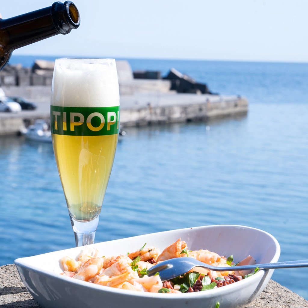 Birrificio Italiano Tipopils being poured into a stemmed glass by a beach.