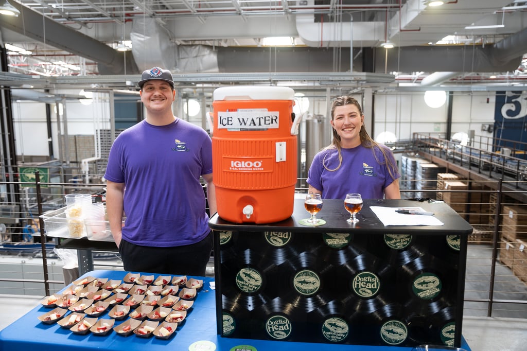 Two people standing by a water cooler with a plate of small bite dishes and a few glasses of beer