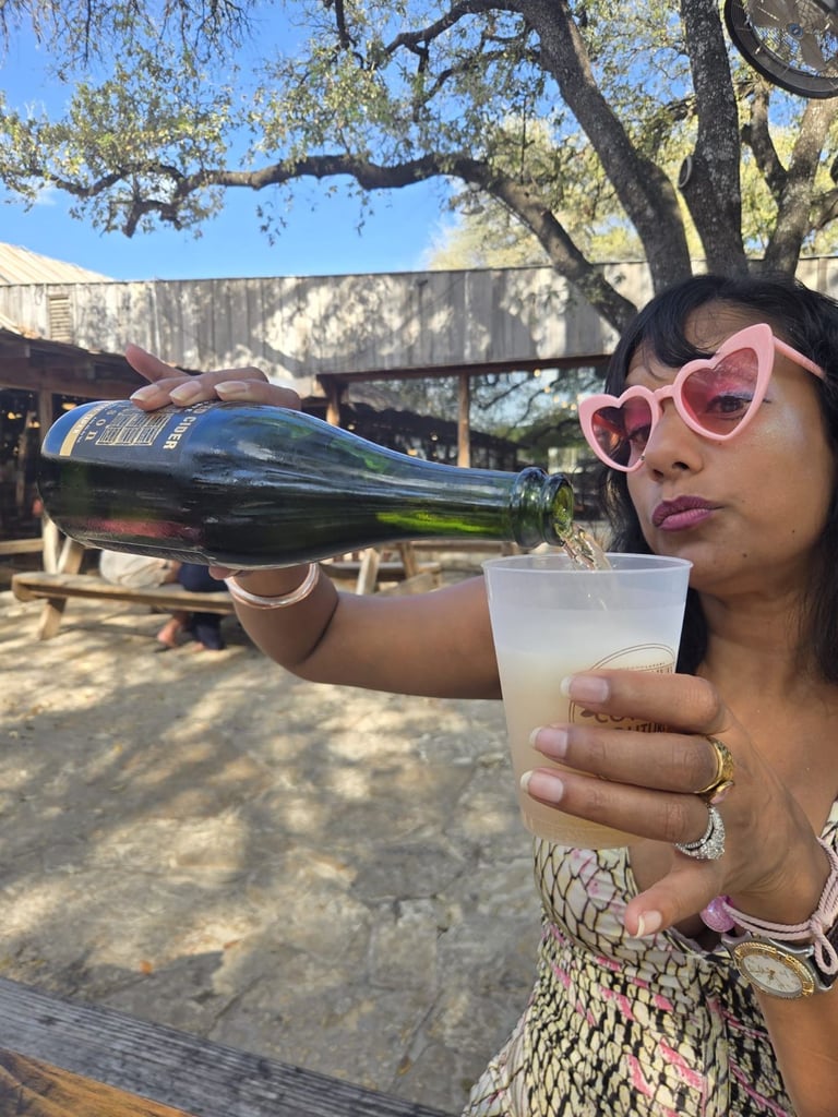 A bottle of Snow Capped Cider “Harrison Reserve” single varietal cider sits on a wooden picnic table, with a plate of barbecue ribs and sides slightly out of focus in the background.