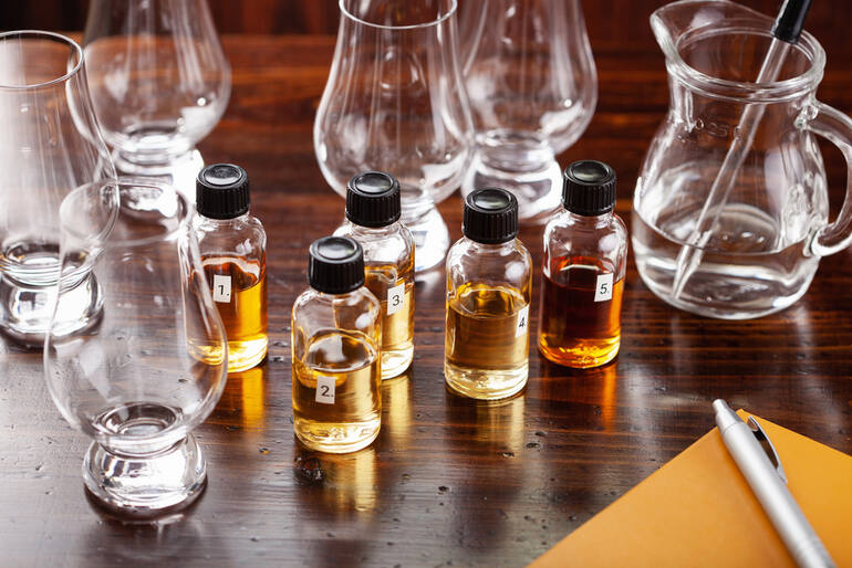 Whisky miniatures and tasting glasses arranged on a wooden table for comparing samples before choosing a full-size bottle.
