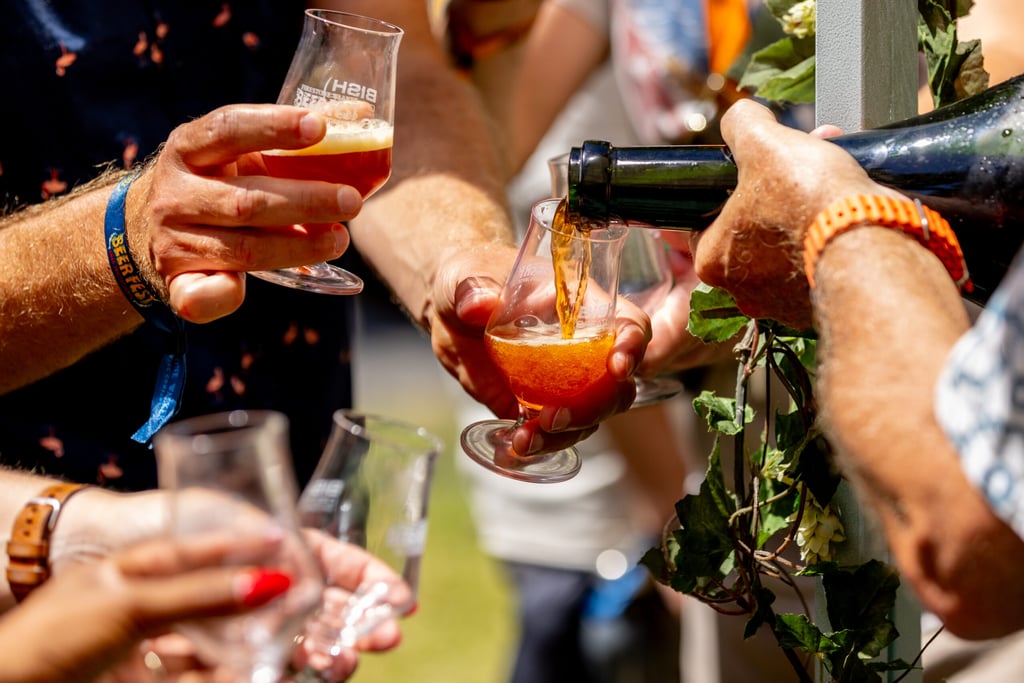 Several glasses of beer being poured into from a large bottle