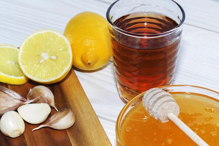 Warm herbal tea with honey, lemon slices, and garlic on a table.