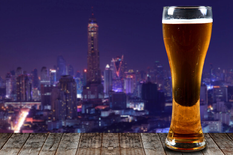 A tall glass of craft beer on a wooden table overlooking a vibrant city skyline at night, representing travel destinations known for craft beer and nightlife in 2026.