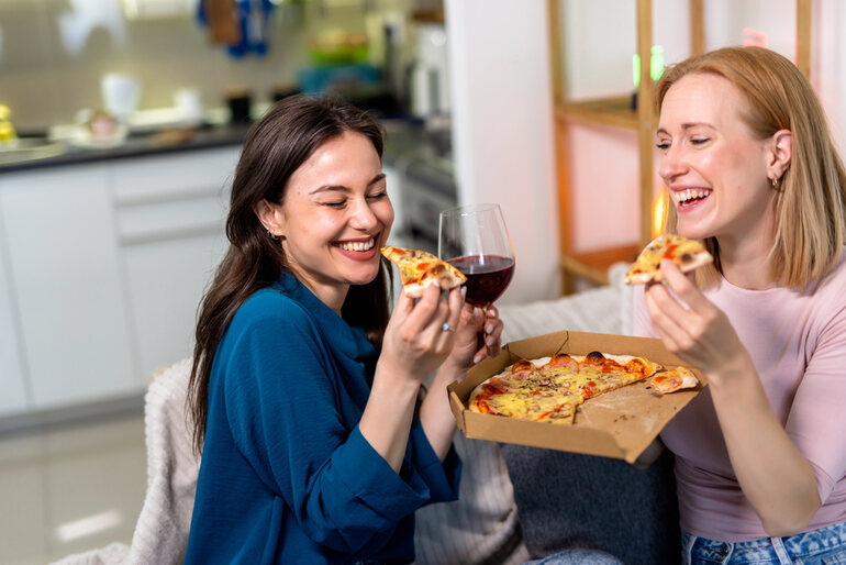 Friends enjoying pizza and red wine during a cozy night in, highlighting relaxing drink choices for a laid-back evening.