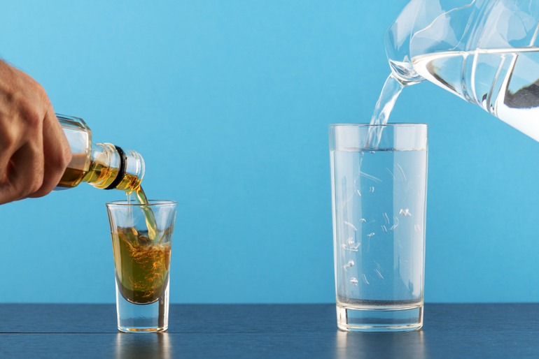 Alcohol being poured into a shot glass beside a THC drink being poured into a tall glass, illustrating the comparison between THC drinks and alcohol.