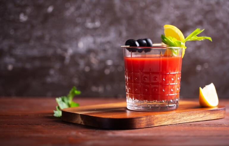 Classic Caesar cocktail garnished with lemon, olives, and herbs, highlighting its history and connection to Canadian brewing culture.