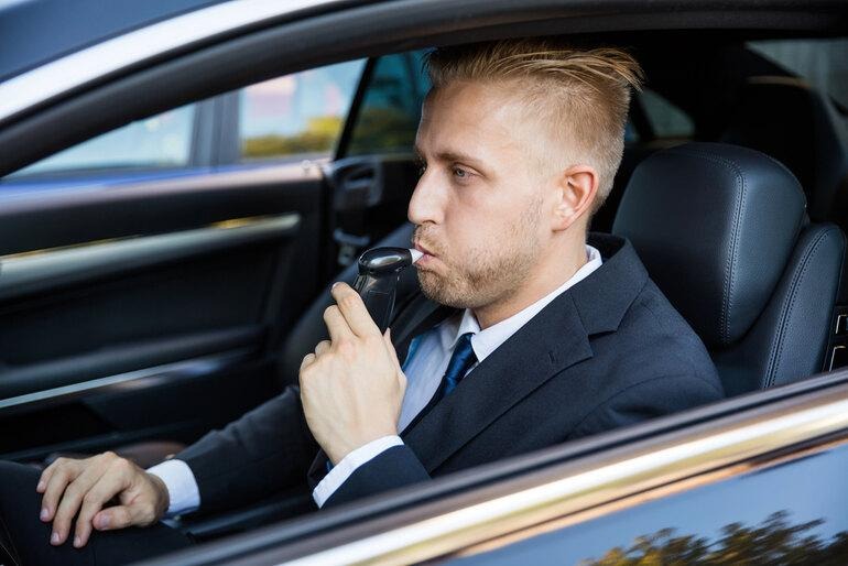 Person performing a breath alcohol test from the driver’s seat, highlighting alcohol and drug testing methods.