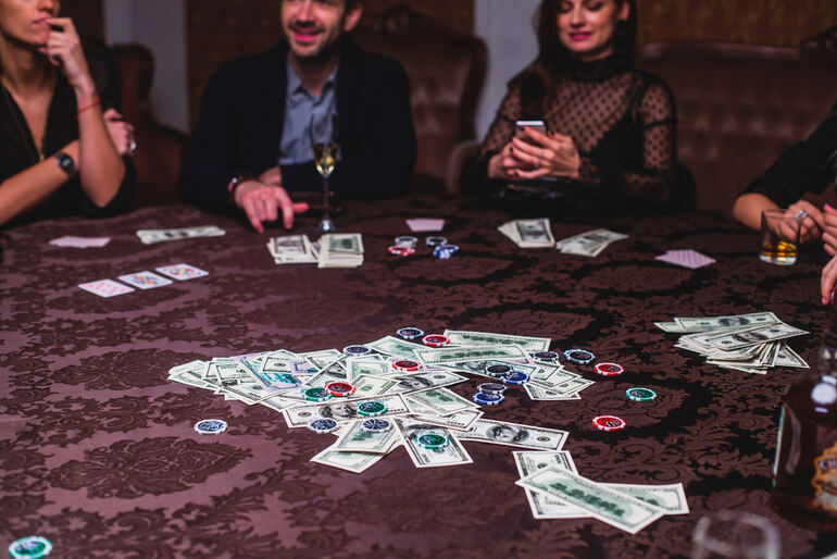 Friends gathered around a poker table with cards, chips, cash, and drinks, creating a simple, social poker drinking game that focuses on fun rather than complicated rules.