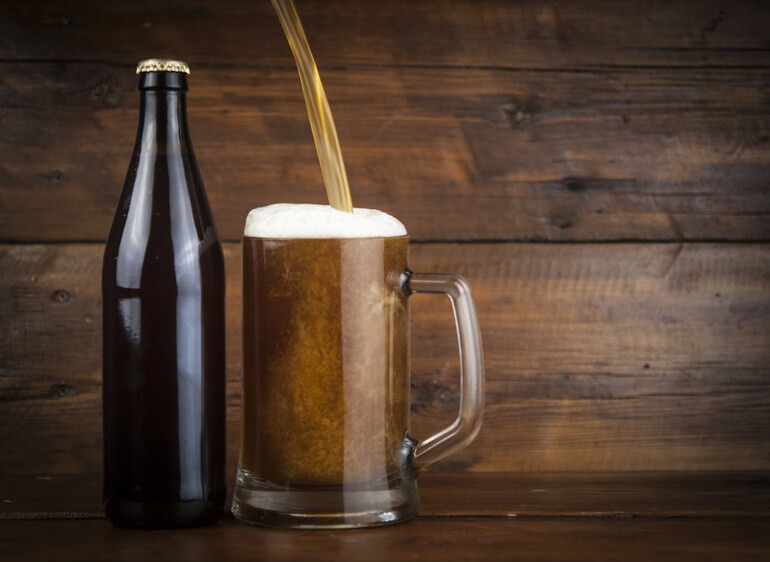Glass mug of beer and dark bottle on a rustic wooden table, representing Canadian beer culture and history.