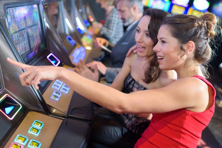 Two women enjoying a slot machine at a casino, highlighting instant, on-the-go gaming access without needing to find a nearby venue.