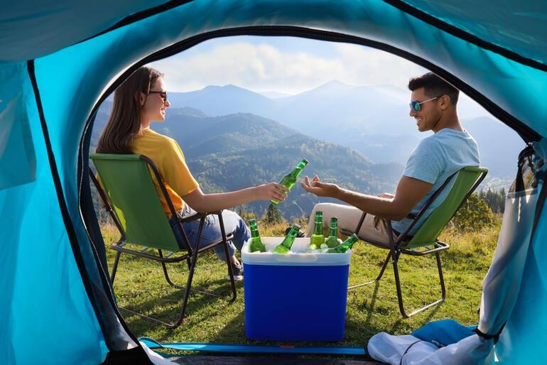 Couple camping beside a cooler full of beer, illustrating a brewery camping weekend with limited cooler space for packing essentials.