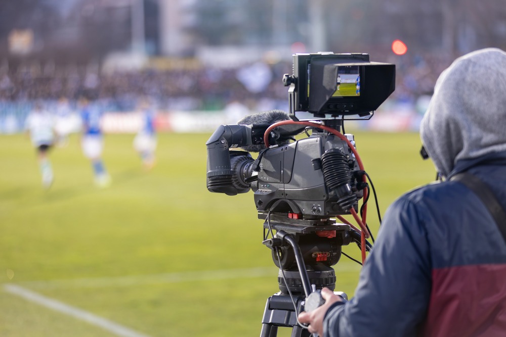 A professional camera operator filming a live soccer match on the field for a sports documentary.