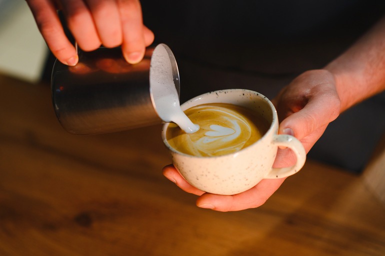 Barista pouring steamed milk into a cup of coffee at an Austin coffee shop.