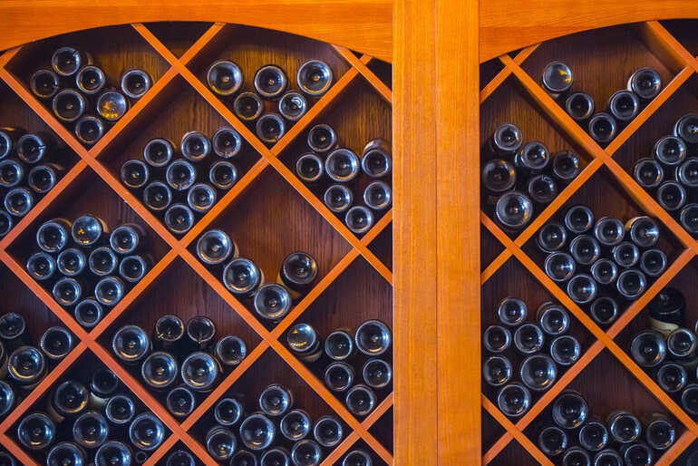 Wine bottles stored horizontally in diagonal wooden racks inside a climate-controlled wine cellar.