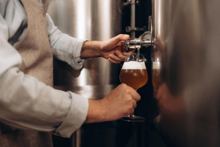 Brewery worker standing at a bar filling a glass with fresh beer from a tap.
