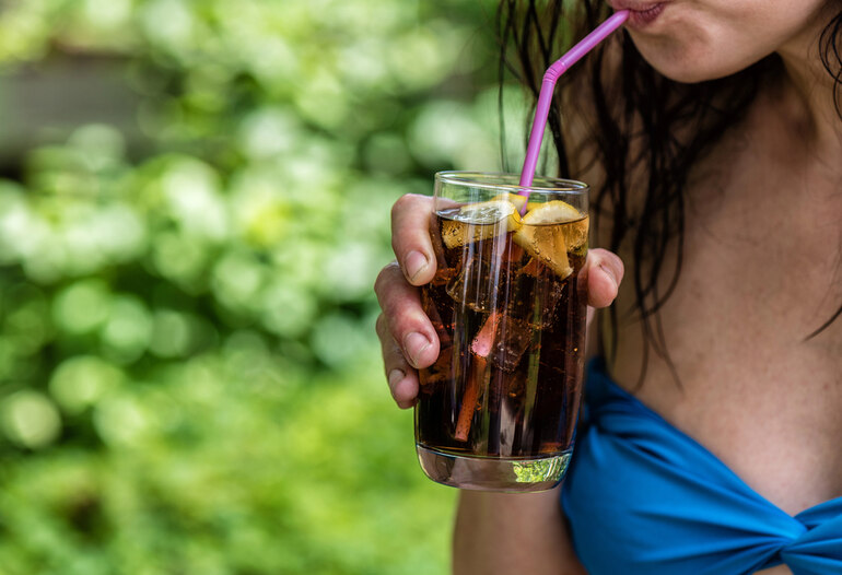 A girl sipping a refreshing iced alcohol-free drink garnished with lemon slices through a straw outdoors.