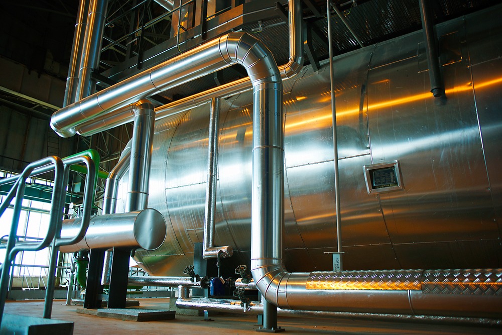Large stainless steel brewery gas storage tank and insulated piping inside a production facility.