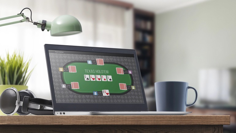 Online poker games displayed on a laptop beside a coffee mug and desk setup.