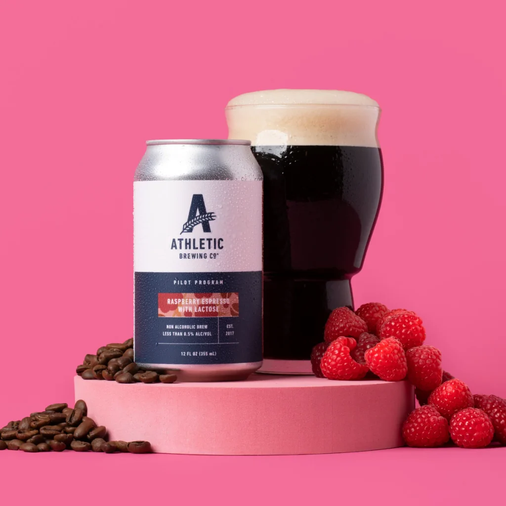 athletic brewing co. raspberry espresso on pink background with coffee beans and raspberries