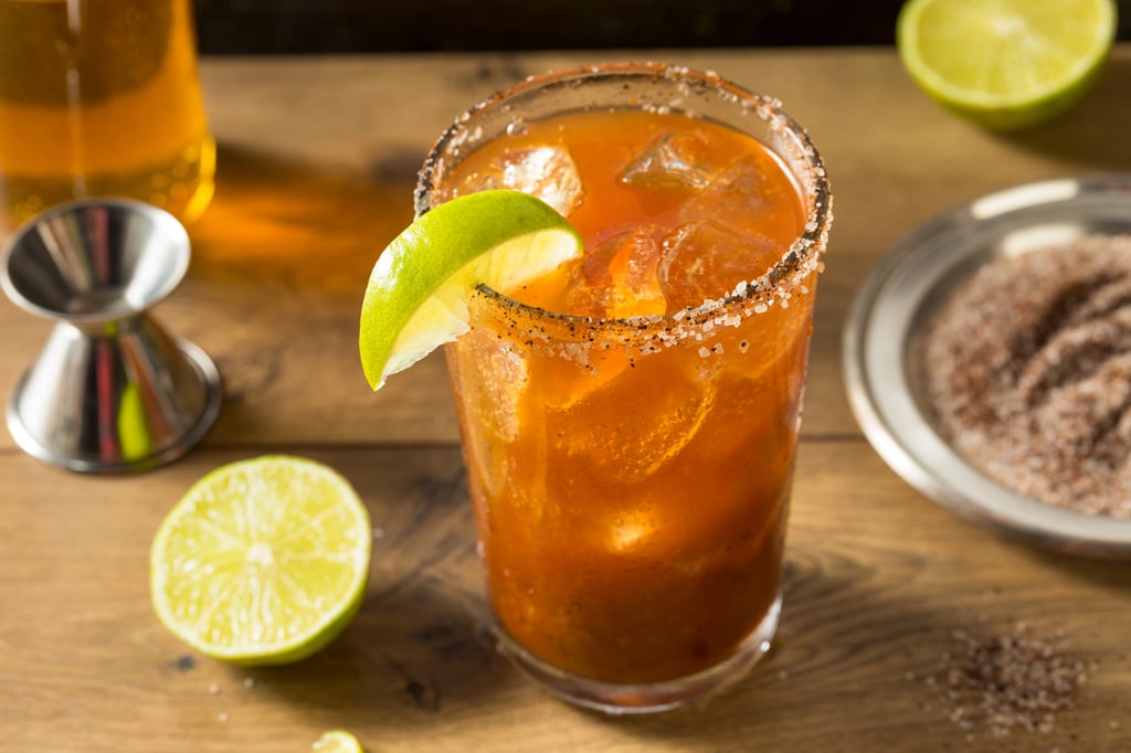 A glass of Tamarind Michelada with a lemon slice and a plate of salt.