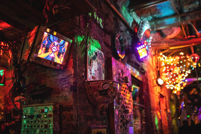 Neon-lit interior of a cluttered dive bar arcade with vintage gaming screens, colorful lights, and a nostalgic atmosphere, reflecting the decline of classic social gaming spaces.