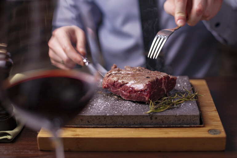 A person cutting a perfectly cooked steak onto a hot stone plate, showing how to enjoy the taste, texture, and presentation of a great steak dining experience.